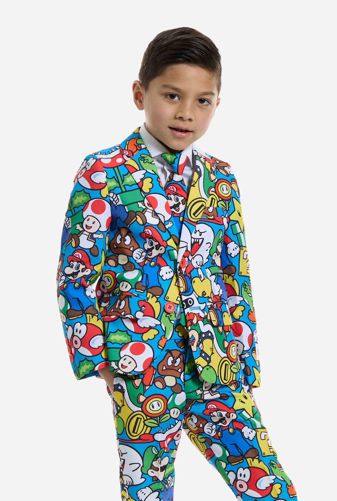 Bild eines Kindes, das einen Anzug mit Super Mario-Allover-Print trägt, bestehend aus Blazer, Hose und Krawatte. Die Hauptfarbe ist blau, aber es gibt auch gelb, rot und weiß.