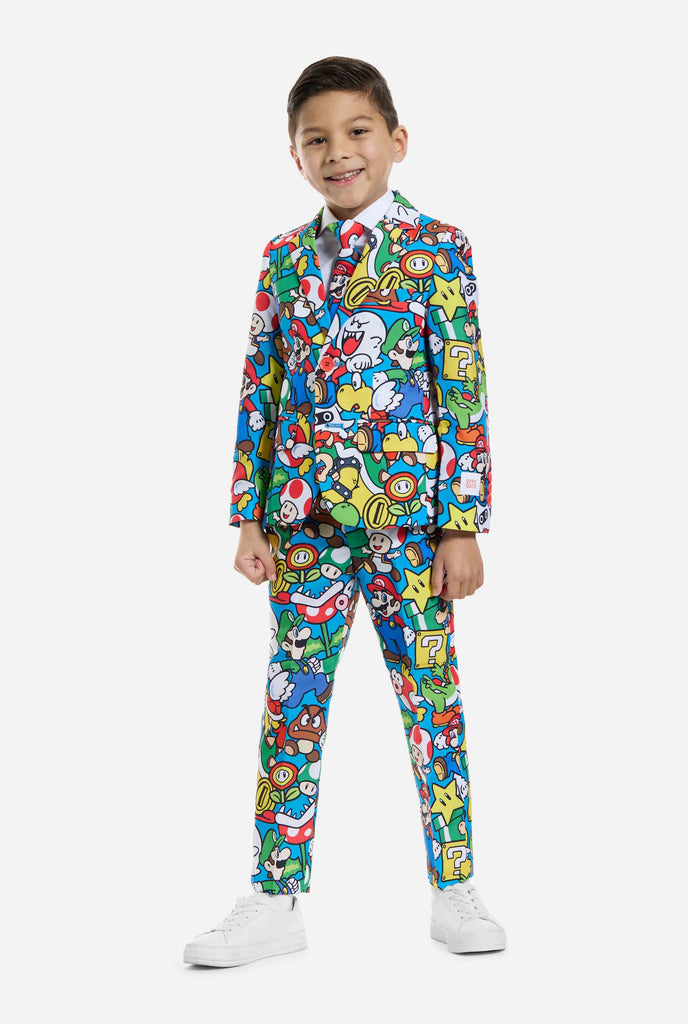 Bild eines Kindes, das einen Anzug mit Super Mario-Allover-Print trägt, bestehend aus Blazer, Hose und Krawatte. Die Hauptfarbe ist blau, aber es gibt auch gelb, rot und weiß.