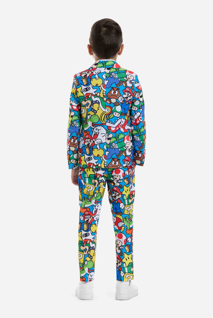 Bild eines Kindes, das einen Anzug mit Super Mario-Allover-Print trägt, bestehend aus Blazer, Hose und Krawatte. Die Hauptfarbe ist blau, aber es gibt auch gelb, rot und weiß.