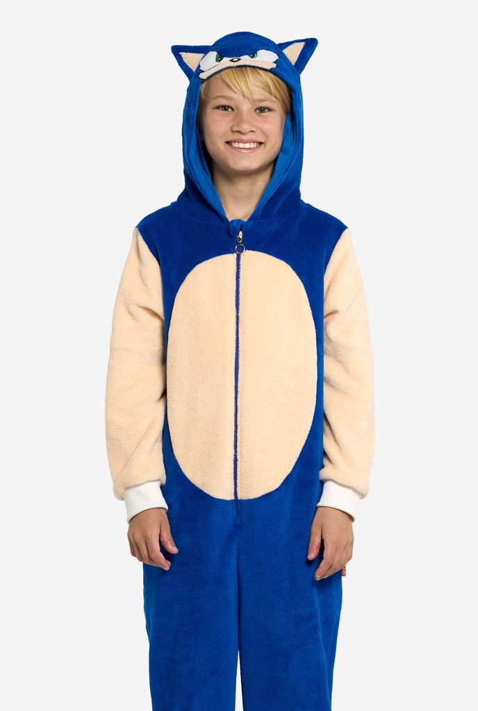 Ein Kind trägt einen verspielten blau-beigen Kinder-Onesie mit Sonic the Hedgehog-Motiv von OppoSuits. Der gemütliche Onesie hat einen Reißverschluss vorne und eine angenähte Kapuze, die Sonics ikonisches Gesicht mit Ohren und ausdrucksstarkem Blick nachahmt. Der blaue Körper des Anzugs bildet einen Kontrast zum beigen Bauch und imitiert Sonics Aussehen. Dieser lustige, bequeme und stylische Strampler ist perfekt zum Entspannen und für Mottopartys und bringt nostalgische Videospielstimmung zu jedem Anlass.