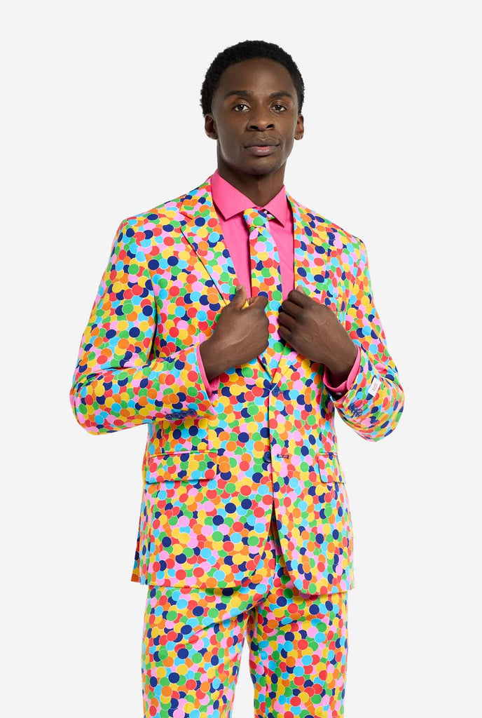 Bild eines Mannes, der einen OppoSuits Confetteroni-Herrenanzug mit Konfetti-Aufdruck und rosa Herrenhemd trägt. Der Anzug besteht aus Hose, Jacke und Krawatte.