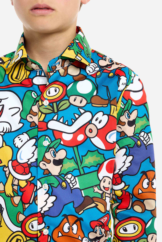 Bild eines Teenagers, der ein T-Shirt mit Super Mario-Allover-Print trägt. Die Hauptfarbe ist Blau, aber es gibt auch Gelb, Rot und Weiß.