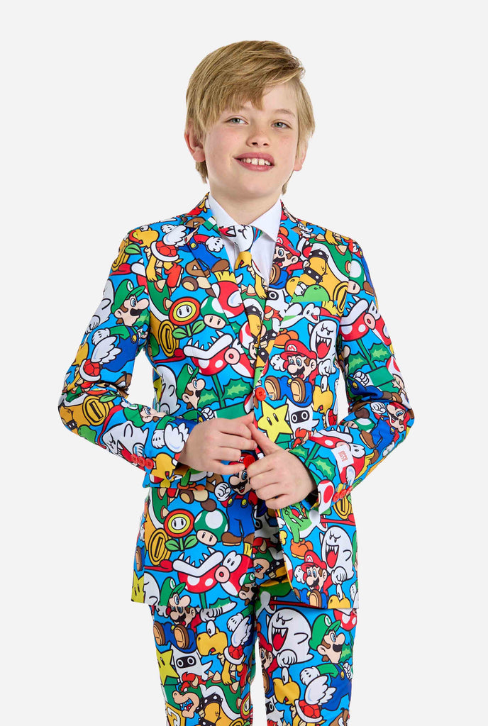 Bild eines Teenagers, der ein Hemd mit Super Mario-Allover-Print trägt, bestehend aus Blazer, Hose und Krawatte. Die Hauptfarbe ist blau, aber es gibt auch gelb, rot und weiß.