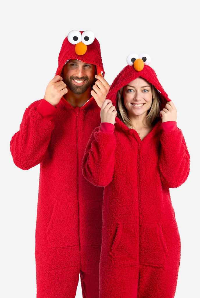 Een man en een vrouw zijn gekleed in een rode Elmo-onesie. Het algehele ontwerp imiteert de look van het Sesame Street-personage Elmo. De achtergrond is effen, waardoor de nadruk op het kostuum ligt.