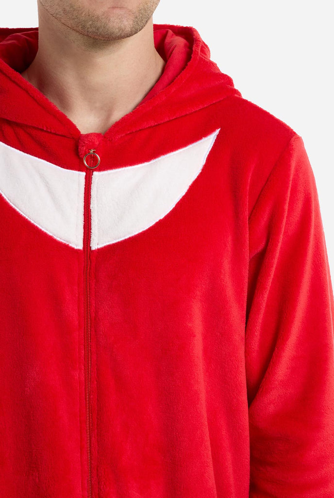 Ein Mann trägt einen leuchtend roten Knuckles the Echidna-Einteiler für Erwachsene von OppoSuits. Der lustige und kuschelige Einteiler verfügt über einen Reißverschluss vorne und eine angenähte Kapuze, die dem Gesicht von Knuckles nachempfunden ist, komplett mit ausdrucksstarken Augen und schlaffen Dreadlocks. Der Anzug ist hauptsächlich rot, mit einem weißen Halbmondmuster auf der Brust, das Knuckles' ikonischen Look aus der Videospielserie Sonic the Hedgehog widerspiegelt.