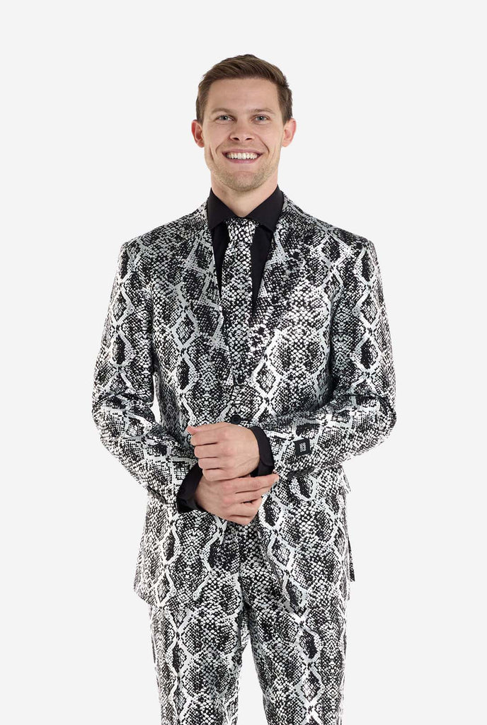 A man is wearing an eye-catching silver and black snake-print suit by OppoSuits. The striking suit features a bold snakeskin pattern, offering a sleek, fashionable look perfect for parties, events, or making a daring fashion statement. The men suit is paired with a black dress shirt and a matching snake-print tie, adding a sophisticated edge to the overall ensemble. The man's confident smile and formal yet modern outfit give off a high-fashion, stylish vibe.