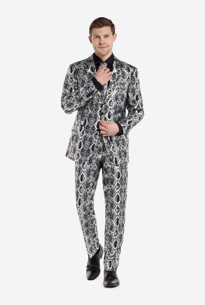 Ein Mann trägt einen auffälligen silber-schwarzen Anzug mit Schlangenmuster von OppoSuits. Der auffällige Anzug weist ein auffälliges Schlangenhautmuster auf und bietet einen eleganten, modischen Look, der sich perfekt für Partys, Veranstaltungen oder ein gewagtes Modestatement eignet. Der Herrenanzug wird mit einem schwarzen Oberhemd und einer passenden Krawatte mit Schlangenmuster kombiniert, was dem Gesamtensemble eine raffinierte Note verleiht.