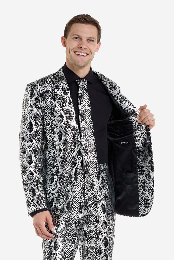 Ein Mann trägt einen auffälligen silber-schwarzen Anzug mit Schlangenmuster von OppoSuits. Der auffällige Anzug weist ein auffälliges Schlangenhautmuster auf und bietet einen eleganten, modischen Look, der sich perfekt für Partys, Veranstaltungen oder ein gewagtes Modestatement eignet. Der Herrenanzug wird mit einem schwarzen Oberhemd und einer passenden Krawatte mit Schlangenmuster kombiniert, was dem Gesamtensemble eine raffinierte Note verleiht.