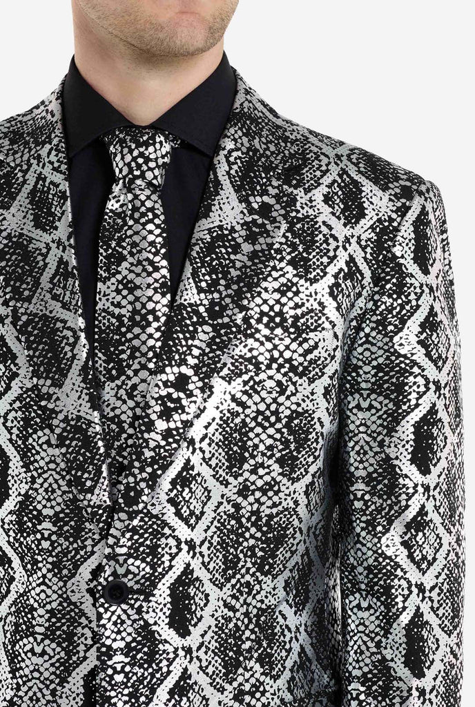 Ein Mann trägt einen auffälligen silber-schwarzen Anzug mit Schlangenmuster von OppoSuits. Der auffällige Anzug weist ein auffälliges Schlangenhautmuster auf und bietet einen eleganten, modischen Look, der sich perfekt für Partys, Veranstaltungen oder ein gewagtes Modestatement eignet. Der Herrenanzug wird mit einem schwarzen Oberhemd und einer passenden Krawatte mit Schlangenmuster kombiniert, was dem Gesamtensemble eine raffinierte Note verleiht.