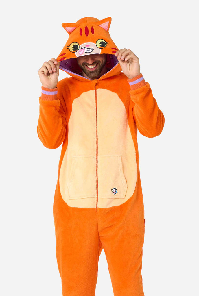 A smiling man is wearing an orange adult onesie designed as a red cat onesie. The onesie features a hood resembling a cat's head, and cat details, perfect for cozy lounging or costume parties. The man is holding the hood over his eyes.