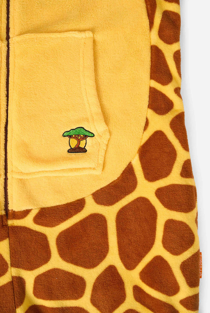 Ein lächelndes Kind trägt einen braun-gelben Kinder Onesie in Form einer Giraffe. Der Onesie hat eine Kapuze, die an den Kopf einer Giraffe erinnert.