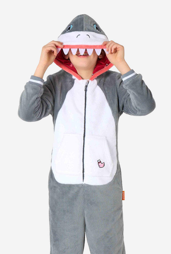 A kid is wearing a grey and white shark kids onesie featuring playful hood details and cozy, soft material, perfect for lounging or costume events. 