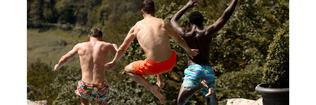 3 Männer in Badeshorts springen in den Pool