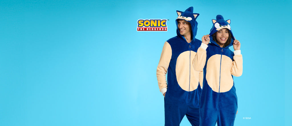 Mann und Frau tragen einen onesie mit Sonic the Hedgehog-Motiv. Blau und Beige, mit Sonics Kopf auf der Kapuze. Das Bild hat ein Sonic-Logo und einen hellblauen Hintergrund.