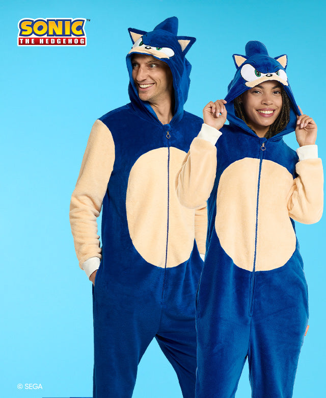 Mann und Frau tragen einen onesie mit Sonic the Hedgehog-Motiv. Blau und Beige, mit Sonics Kopf auf der Kapuze. Das Bild hat ein Sonic-Logo und einen hellblauen Hintergrund.